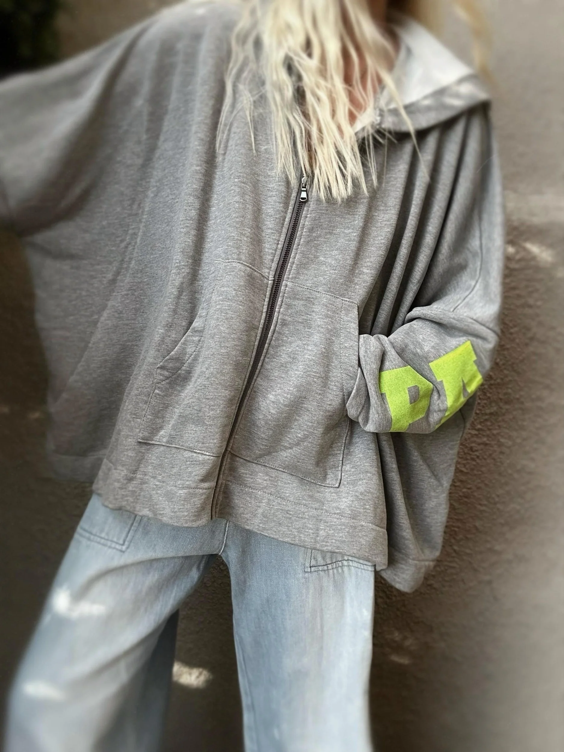 Woman wearing the grey Banditas Paradise zip-up sweatshirt with light blue jeans