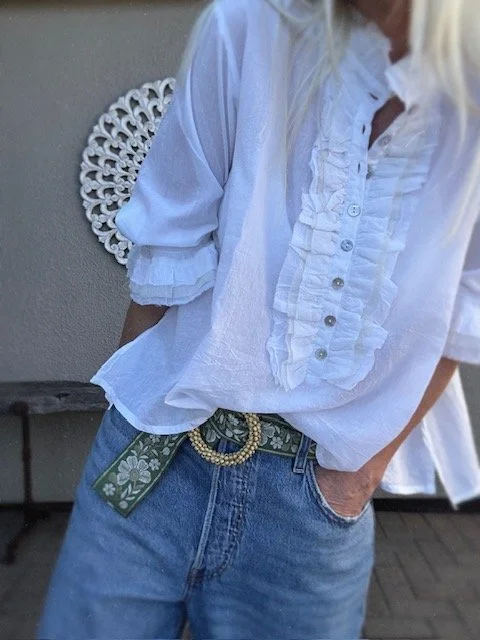 Green embroidered floral belt with cream flowers and a gold beaded oval buckle, styled on a wooden stool.