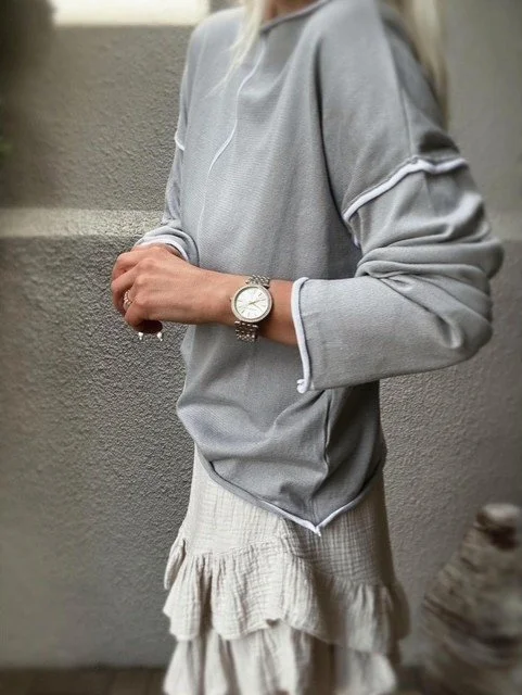 Three-quarter front view of the Wren Long Sleeve Knit in grey with white contrast piping along seams and cuffs.