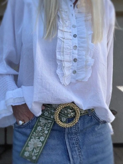 Green floral belt with gold-tone beaded buckle on a wooden surface.