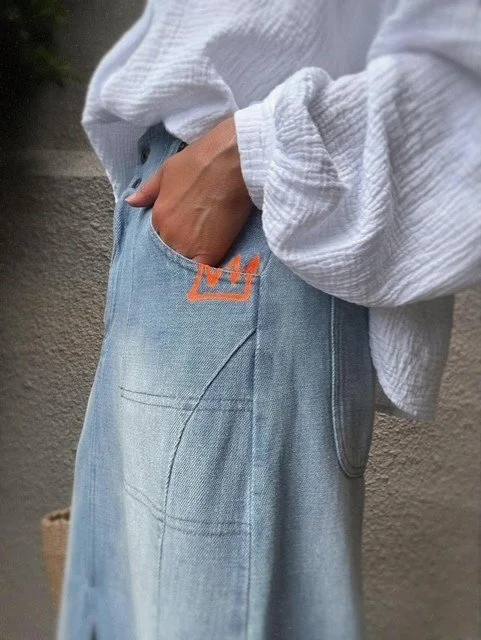 Banditas Collatino Skirt in light-wash denim, hand in pocket showing the neon orange crown embroidery.