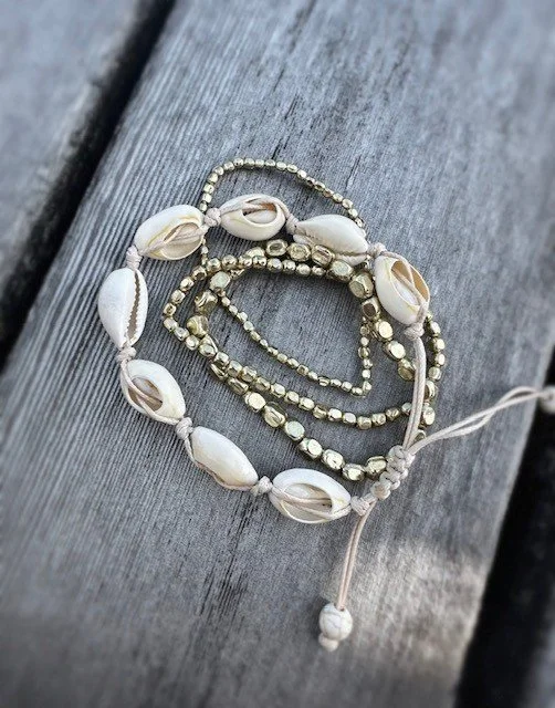 Stacked cowrie shell and gold nugget bracelets styled for an everyday coastal look
