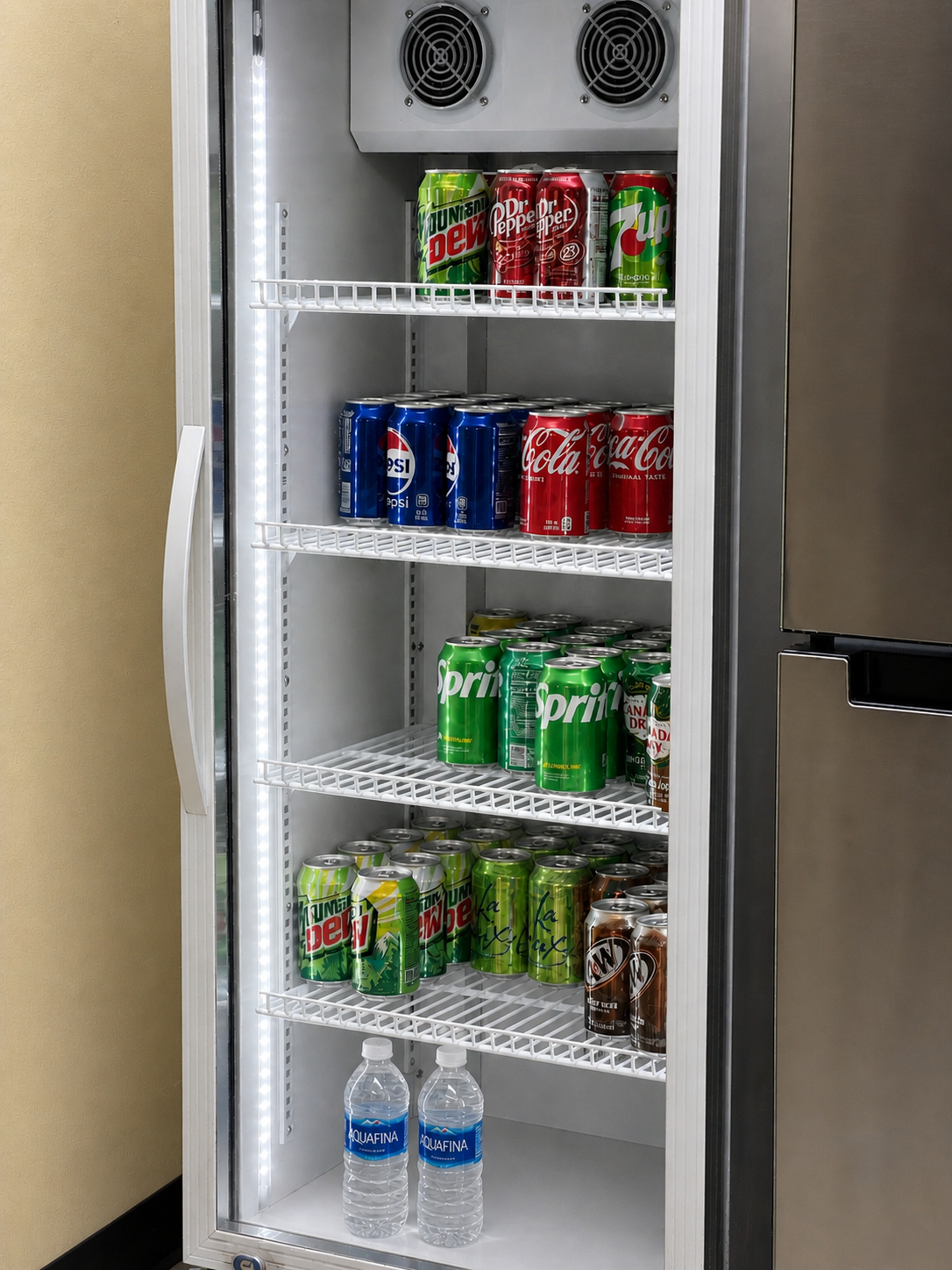A vending refrigerator stocked with cans of Sprite, Coca-Cola, Dr. Pepper, Mountain Dew, 7-Up, Diet Mountain Dew, and bottled Aquafina water.
