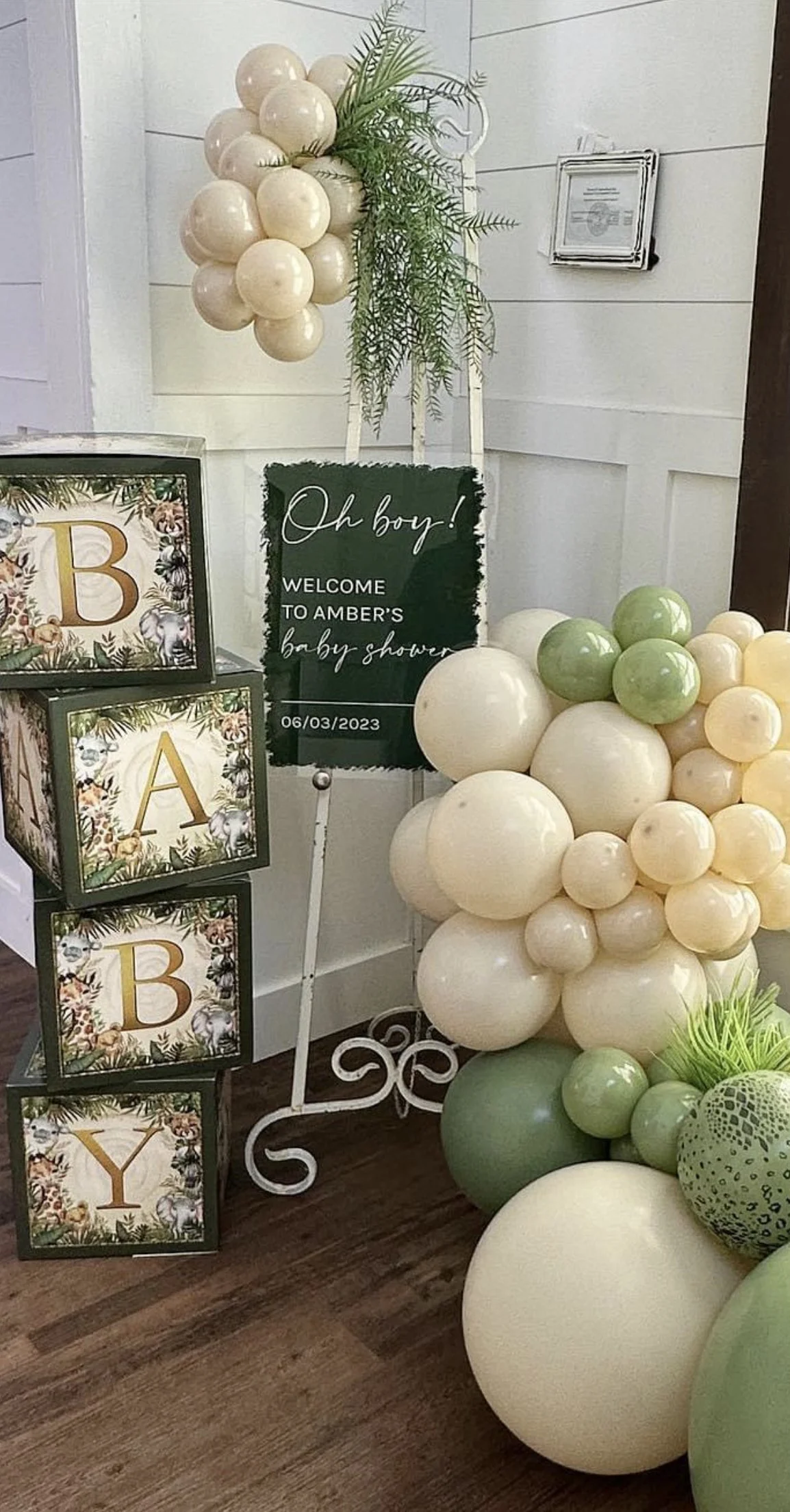 Decorative balloon arrangement in pale yellow, green, and white surrounding welcoming signs for a baby shower event.