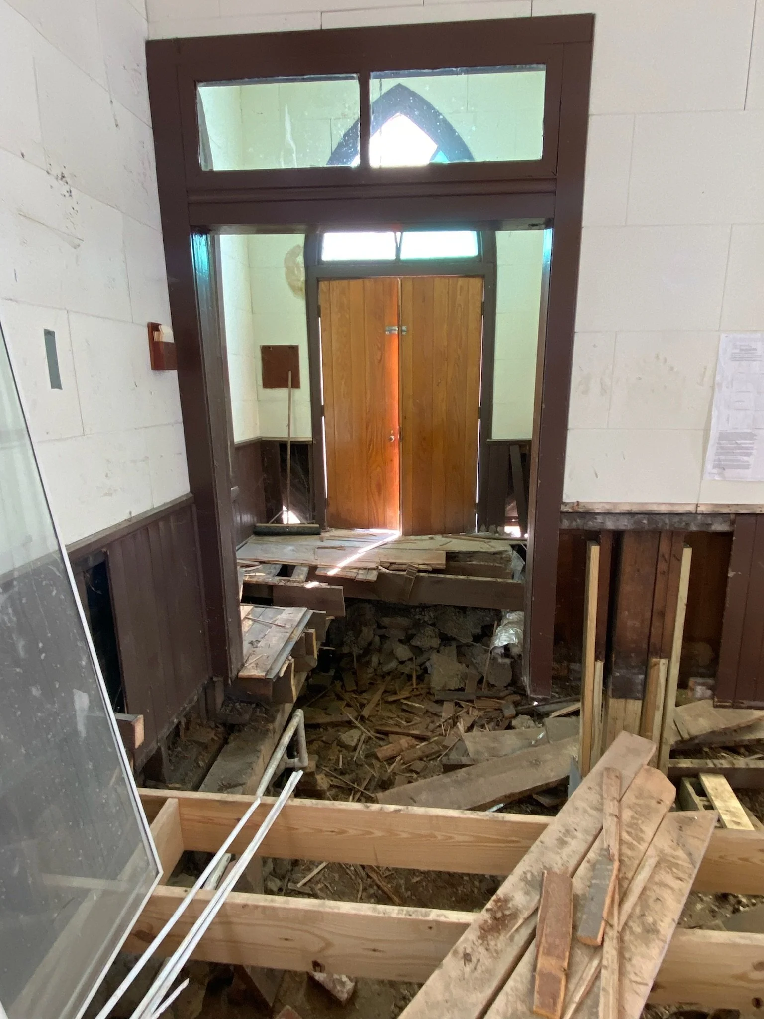Interior of a building under renovation with exposed flooring, insulation, and wood framing, appearing to be a doorway area.