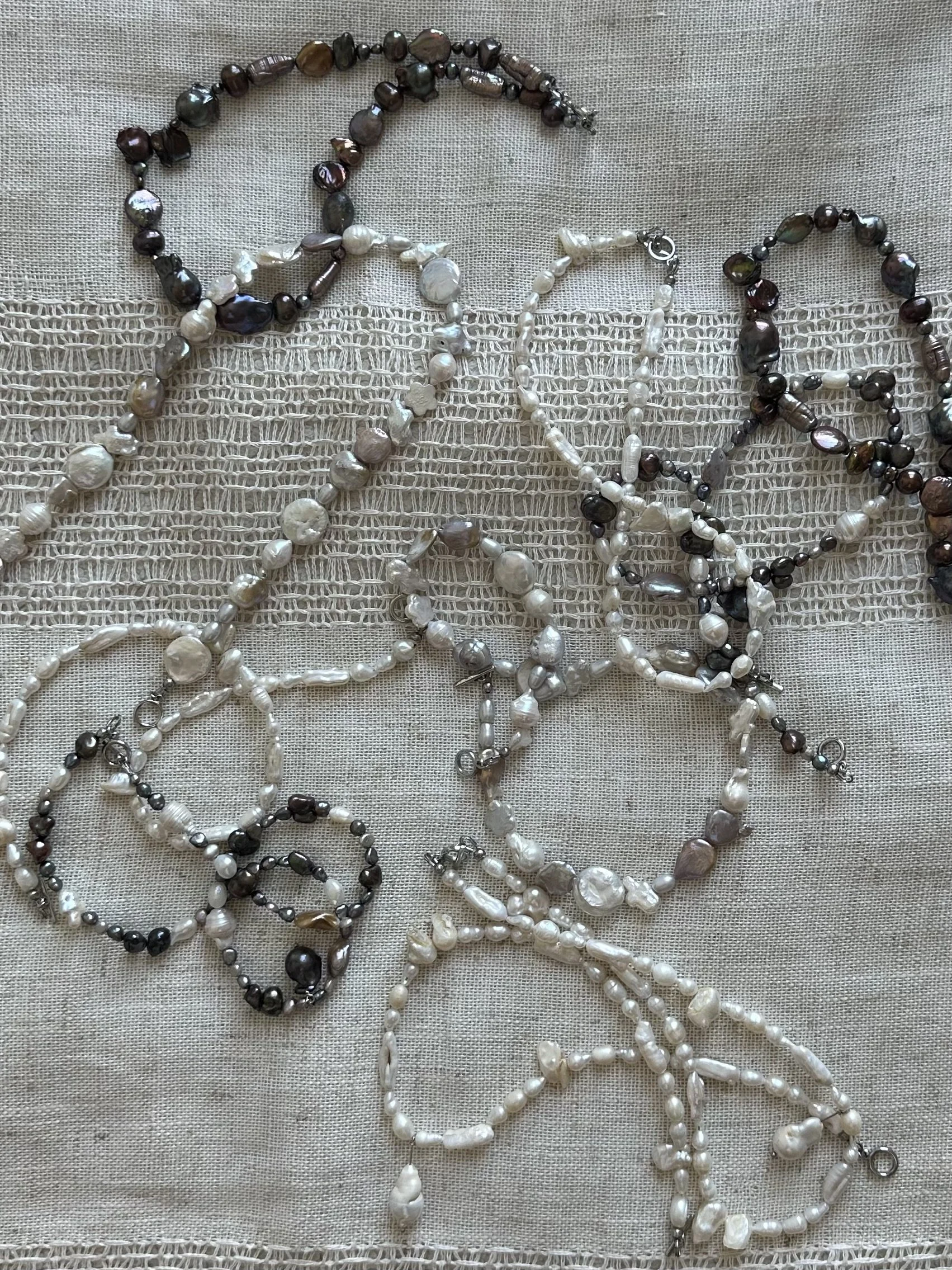 Multiple pearl and gemstone necklaces and jewelry laid on a beige fabric background.