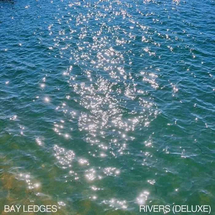 Sparkling water with sunlight reflections on the surface, near a shoreline. Text on image says 'BAY LEDGES' and 'RIVERS (DELUXE).'
