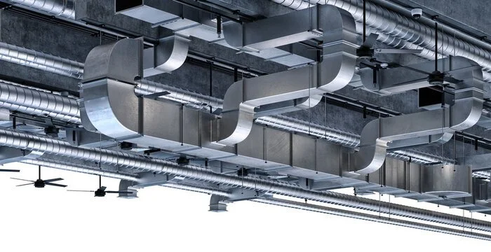 Industrial ceiling with large metal air ducts, ventilation pipes, and ceiling fans.