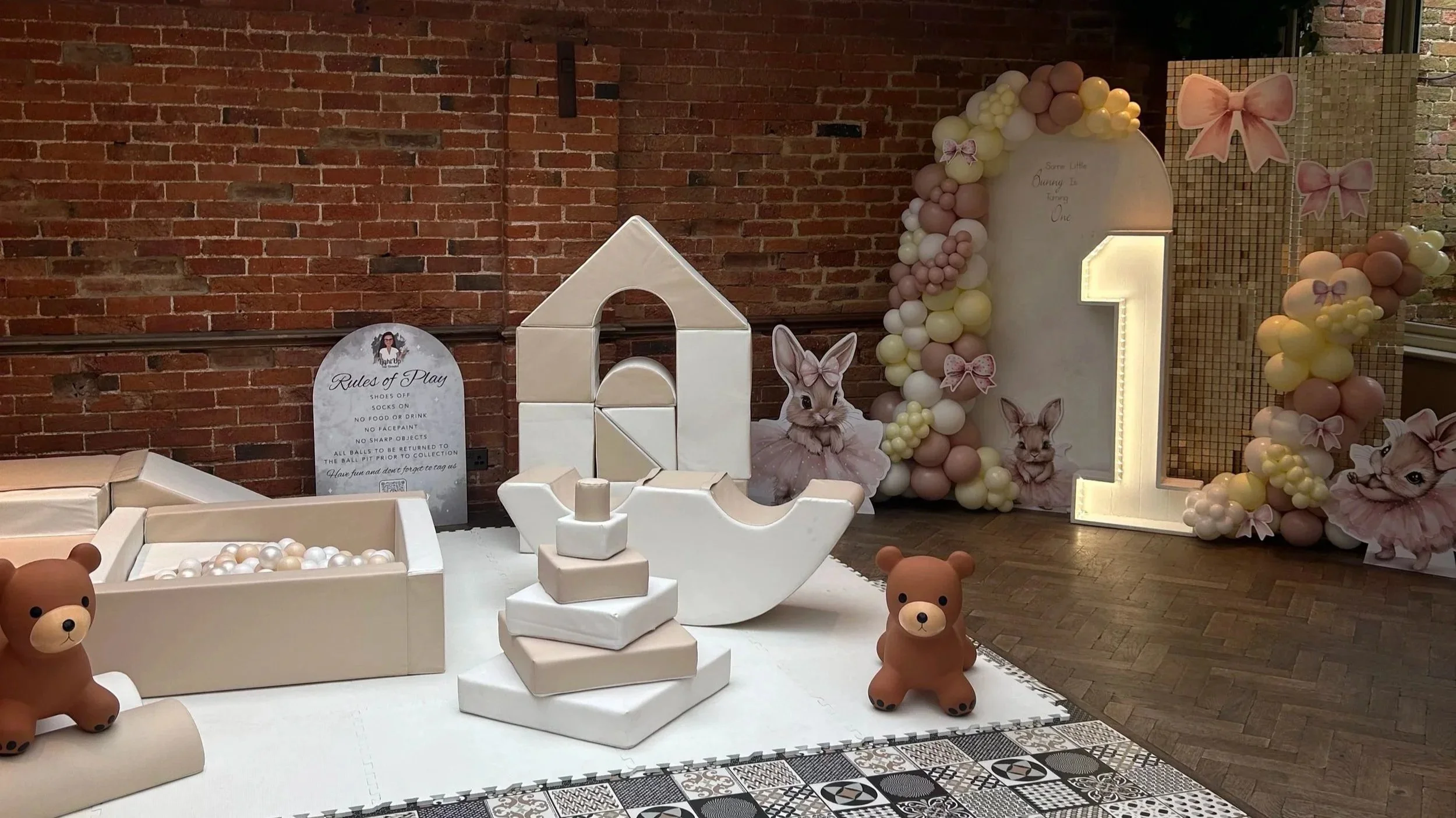 Decorative setup with balloons, bunny cutouts, and teddy bear figures for a children's party or baby shower, featuring a brick wall background.