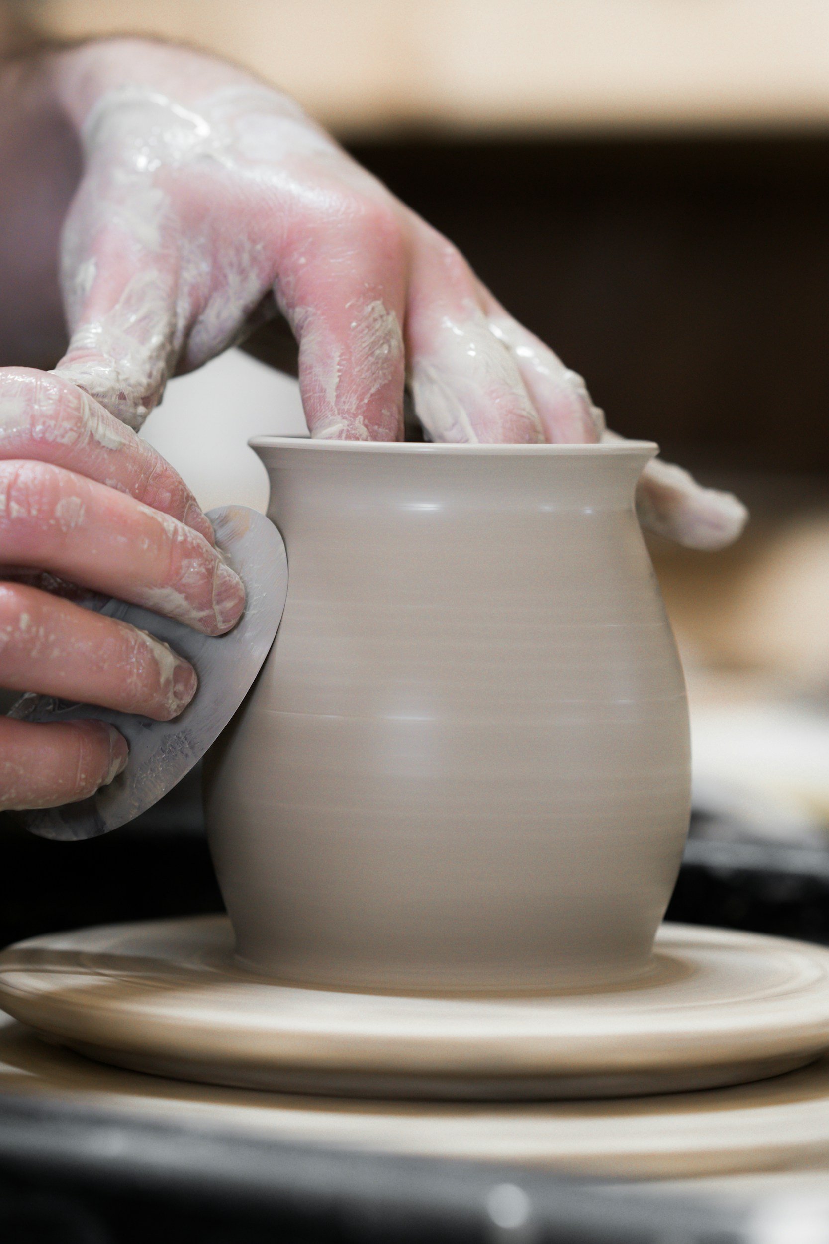 Close-up of a person's hand shaping a ceramic pot on a pottery wheel, with clay on fingers.
