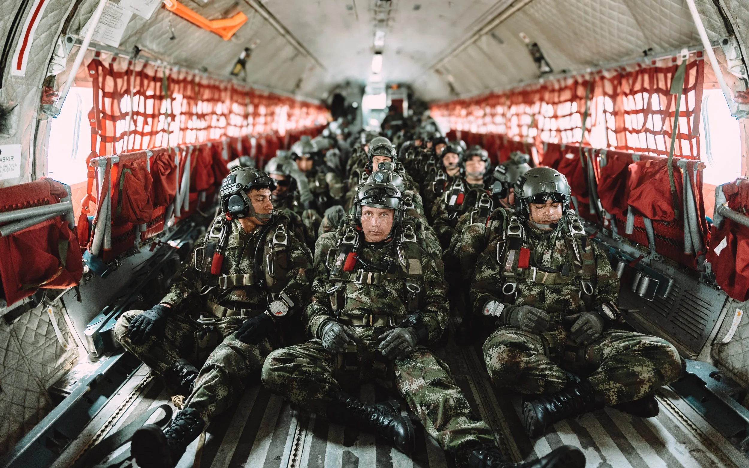 Soldiers in full gear seated shoulder to shoulder inside an aircraft cabin, waiting