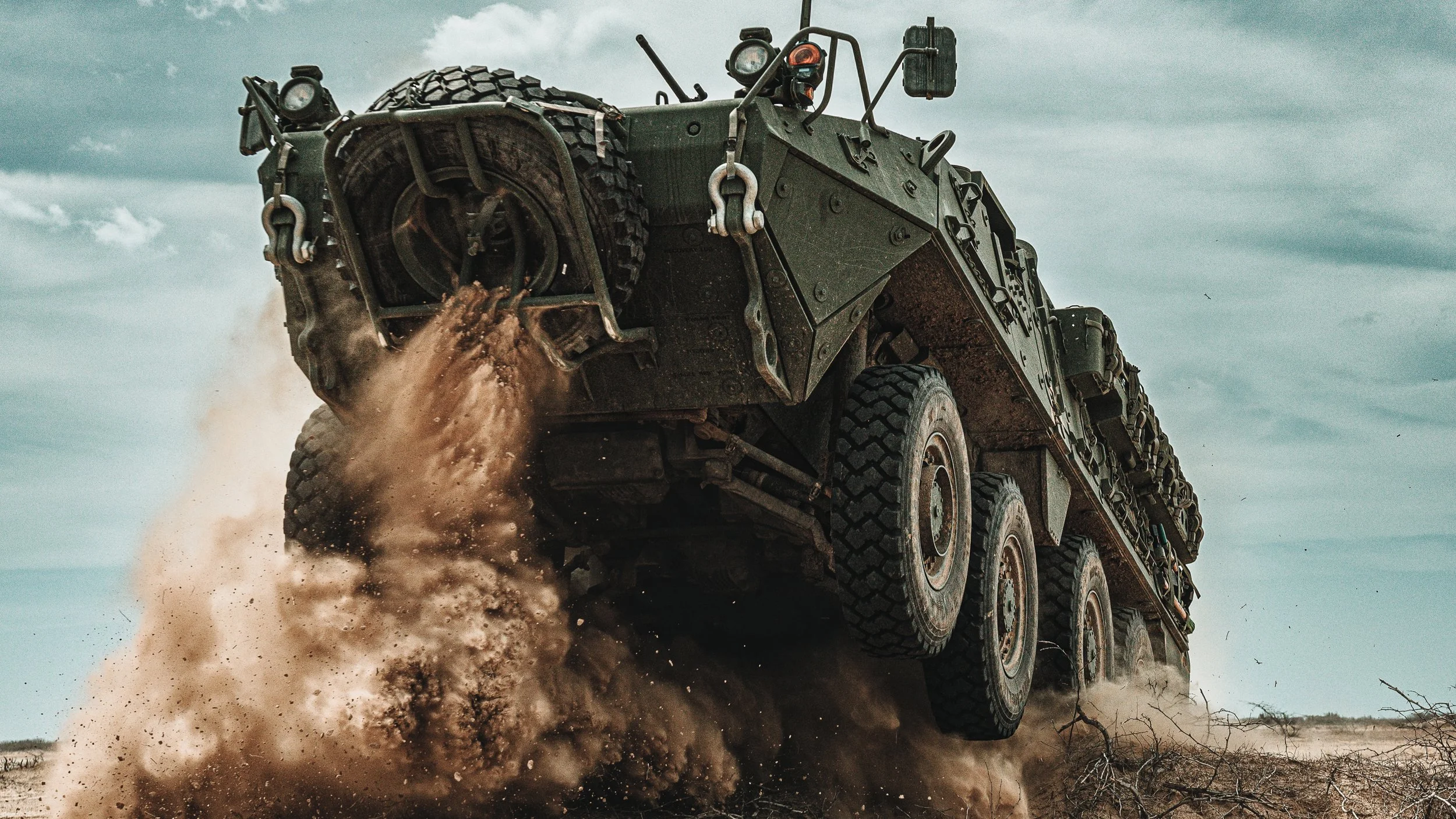 Armored vehicle crossing dry ground, dust rising behind it