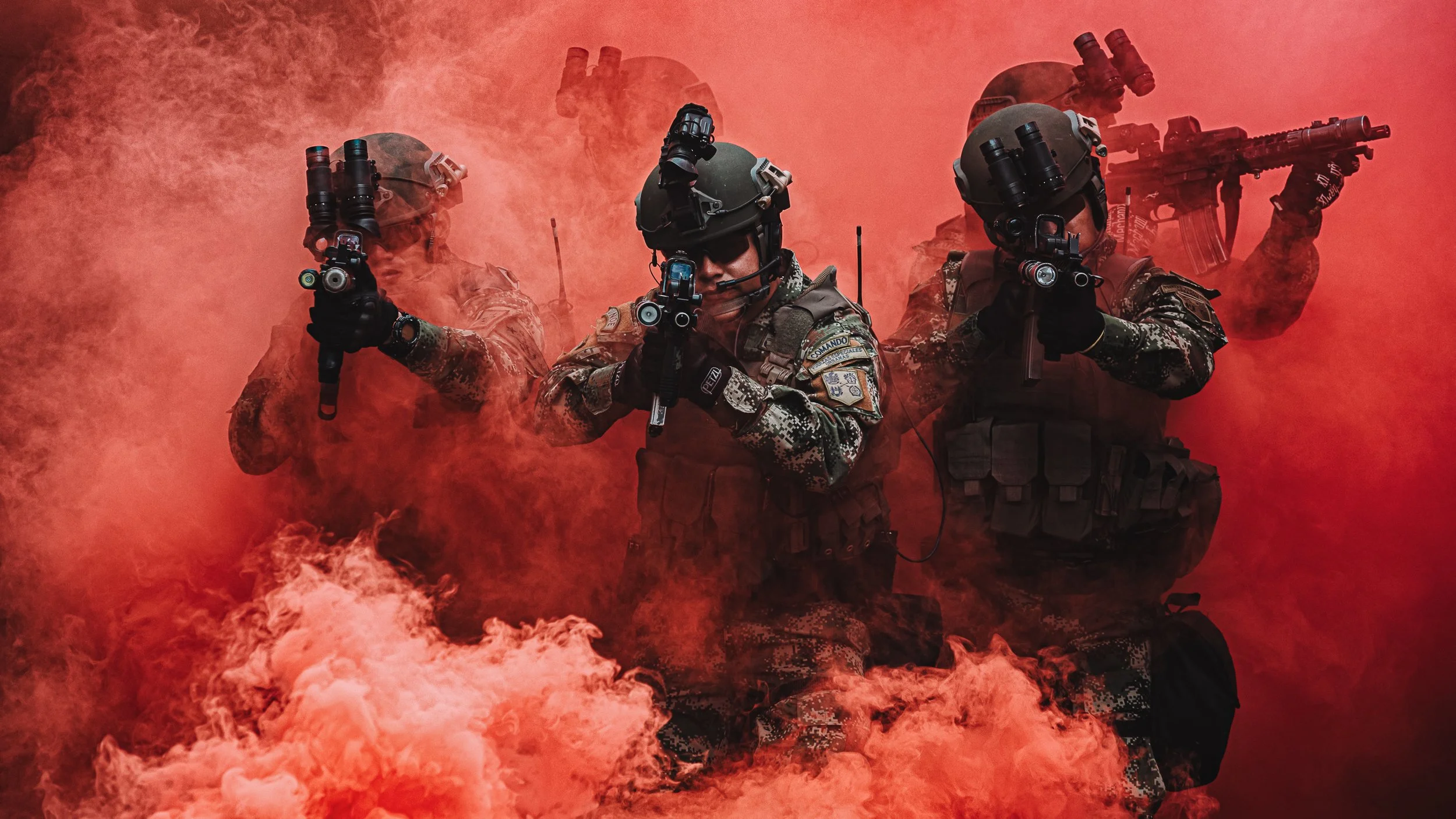 Three soldiers in night-vision helmets and tactical gear standing in red smoke