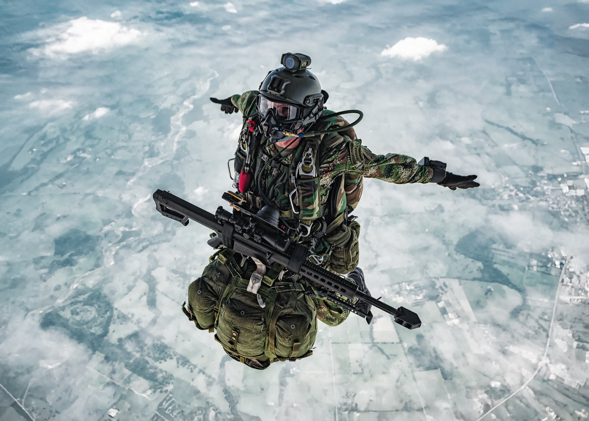 Soldier in freefall above snow-covered ground, arms spread, rifle across his body