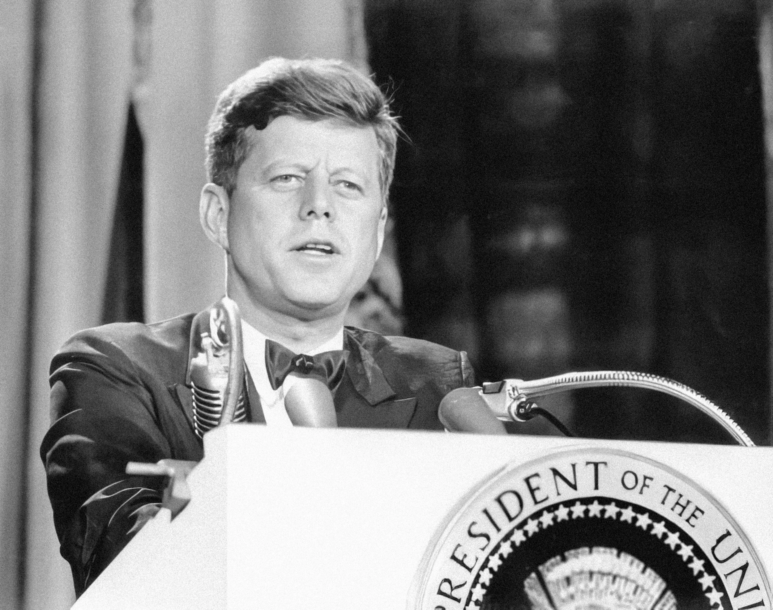 Black-and-white photo of a woman speaking at a podium with a seal of the United States on it.