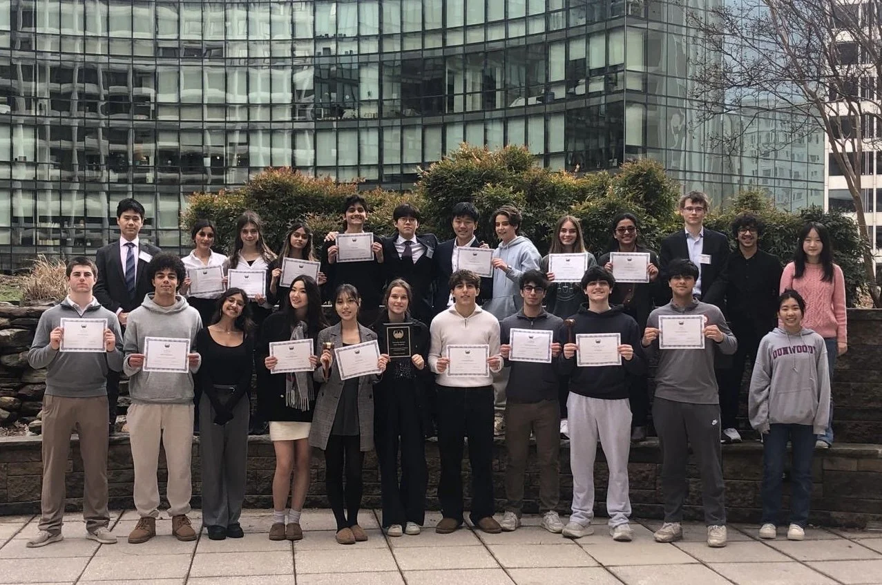Group of students holding certificates outside in an urban area with a glass building in the background.