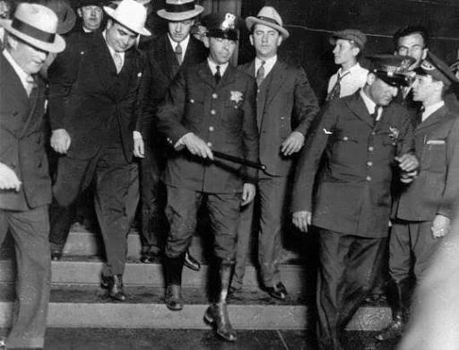 Group of men, some in police uniforms, descending stairs during a historical event, black and white photograph.