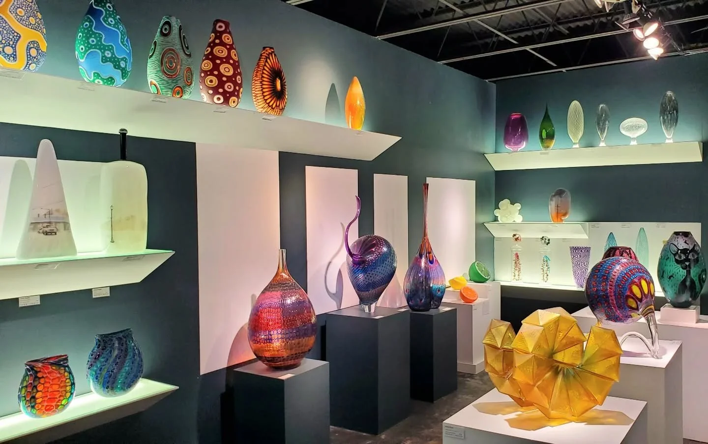 Display of colorful glass sculptures and vases in an art gallery.