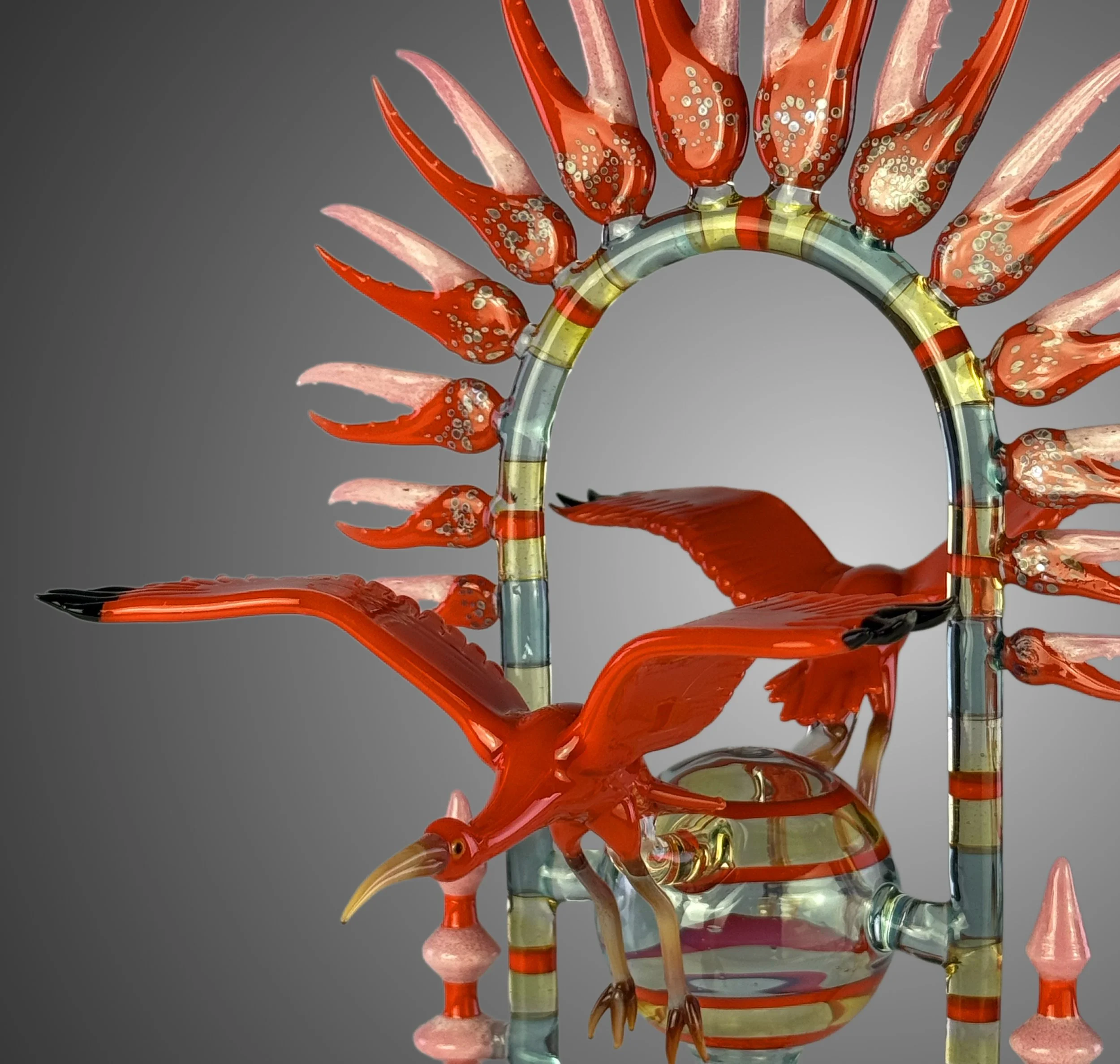 Colorful glass sculpture resembling a flower with red, pink, yellow, and blue hues, set against a gray background.