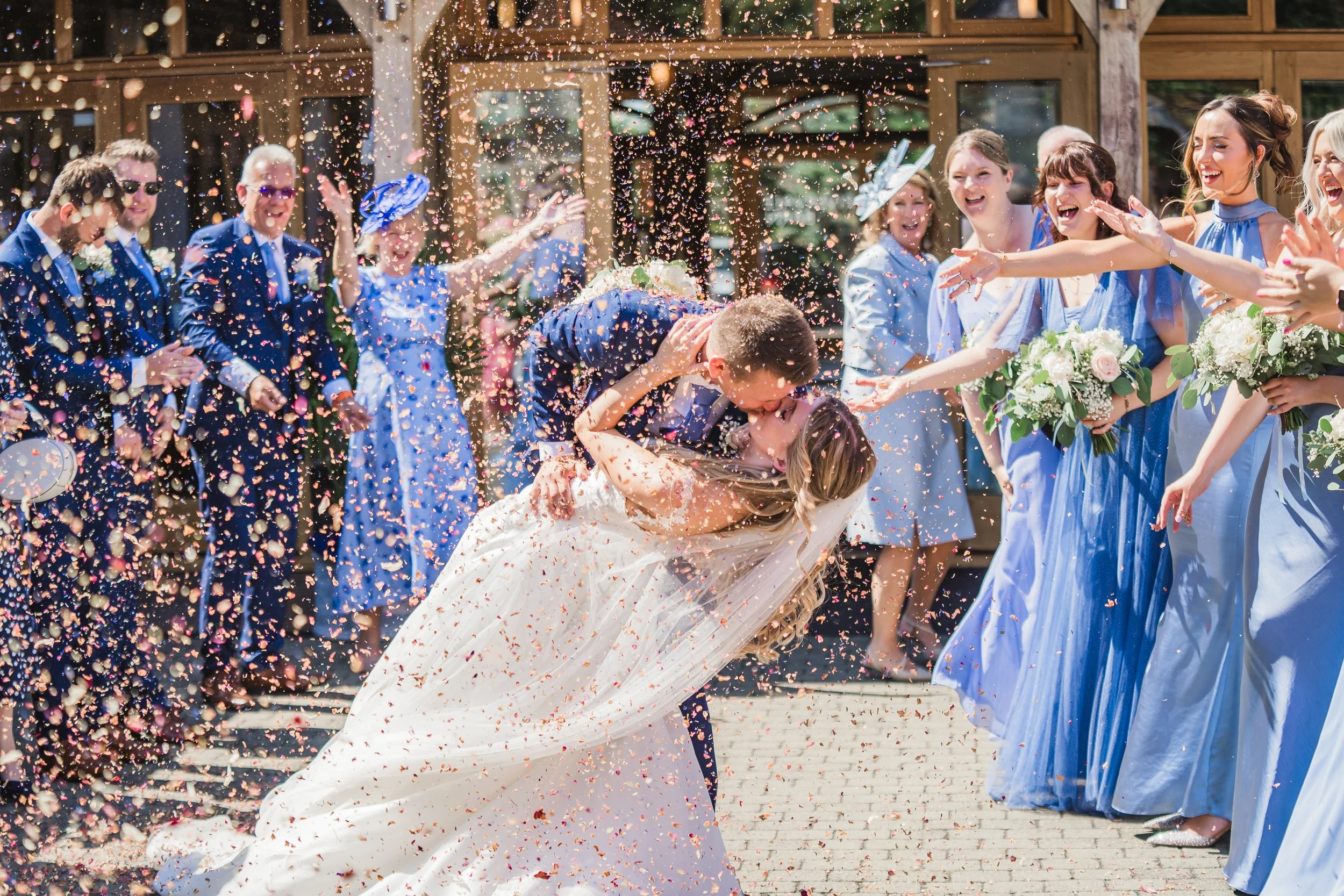 A wedding celebration with guests throwing colorful confetti at a bride and groom hugging.