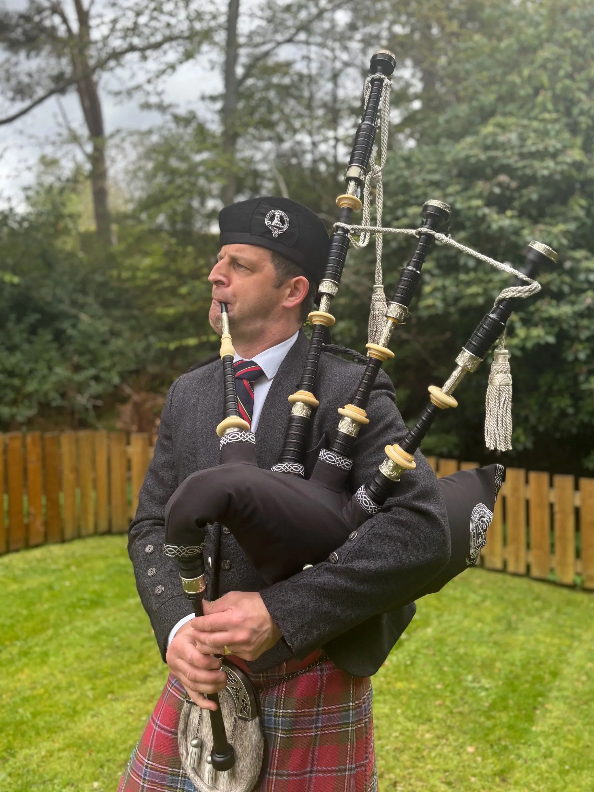 A man dressed in traditional Scottish attire playing the bagpipes outdoors.