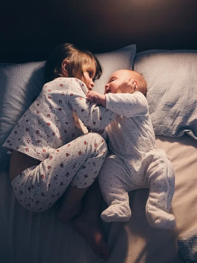 Two young children in pajamas lying on a bed, cuddling and gazing at each other.