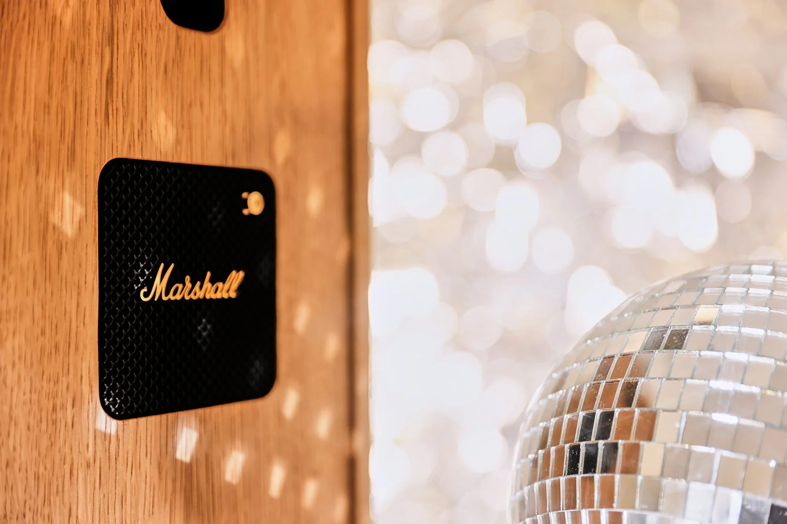A black Marshall speaker on a wooden surface next to a disco ball with a background of sparkling lights.