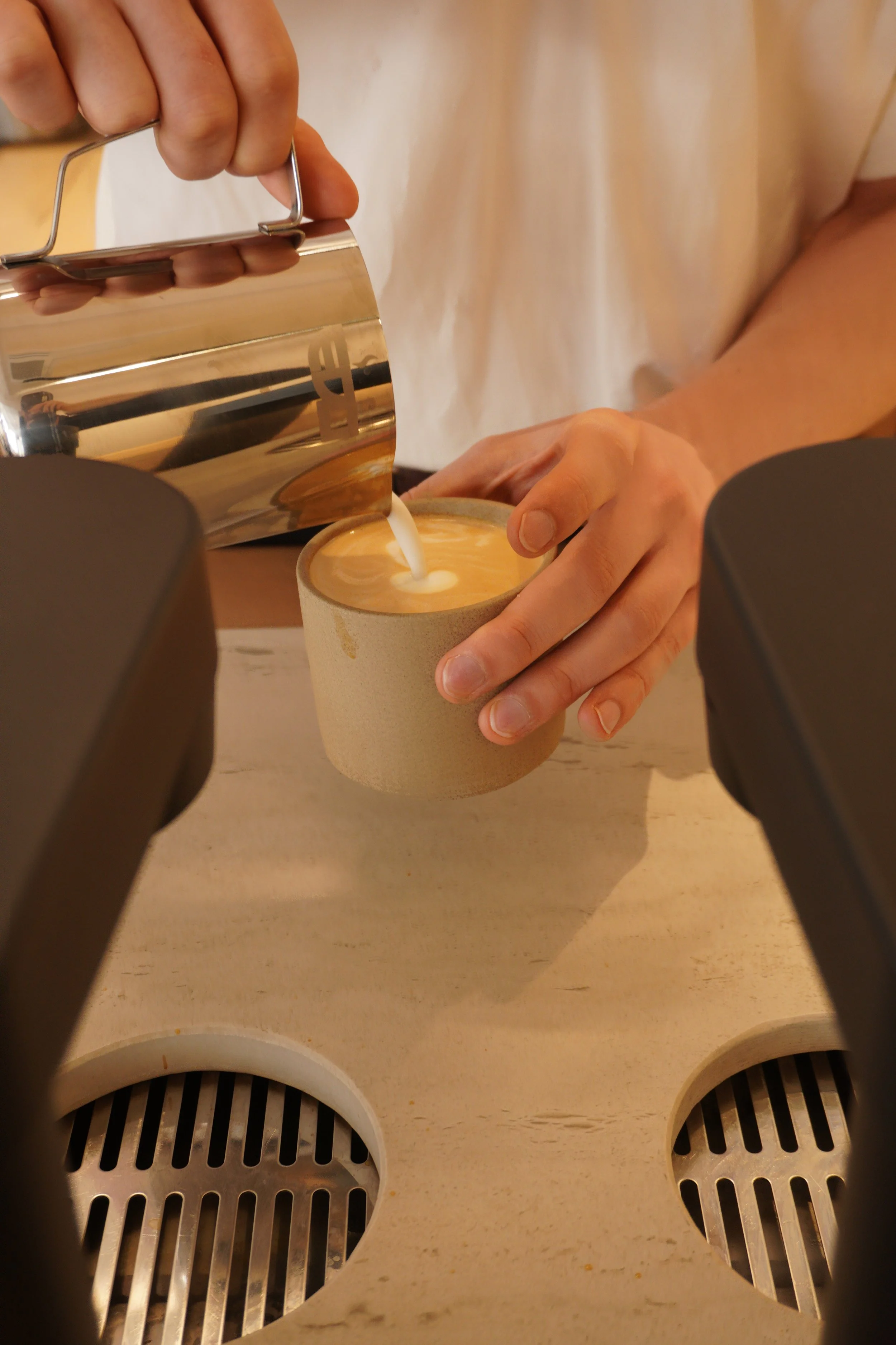 Close-up of a person pouring steamed milk into a cup of espresso, creating a latte art in a coffee shop.
