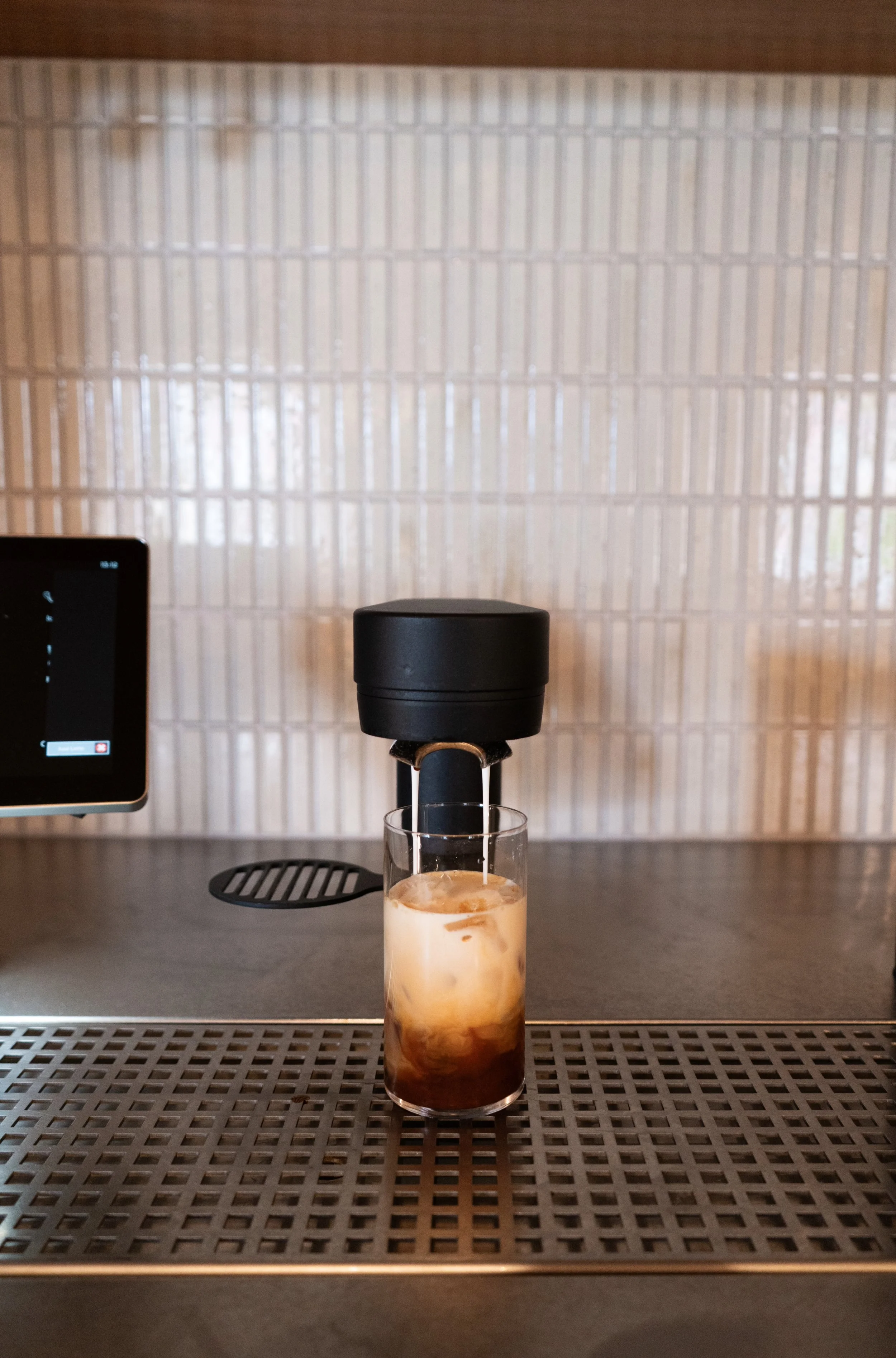 A glass of iced coffee or latte with milk and ice cubes in front of an under-counter coffee solution