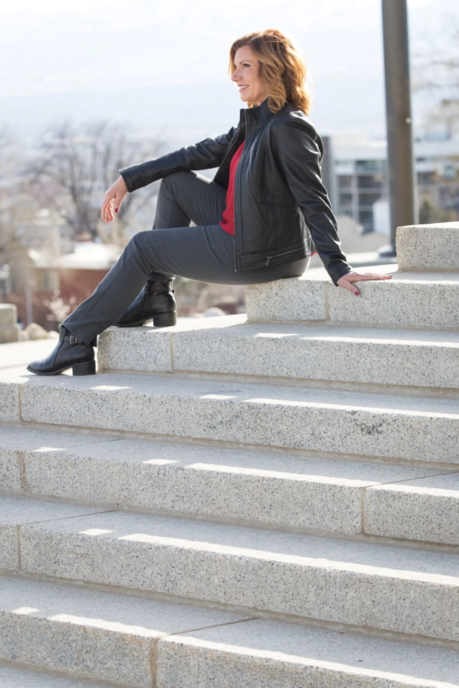 maureen farrell in black jacket and red blouse  sitting on marble steps under flagpole smiling while overlooking the city