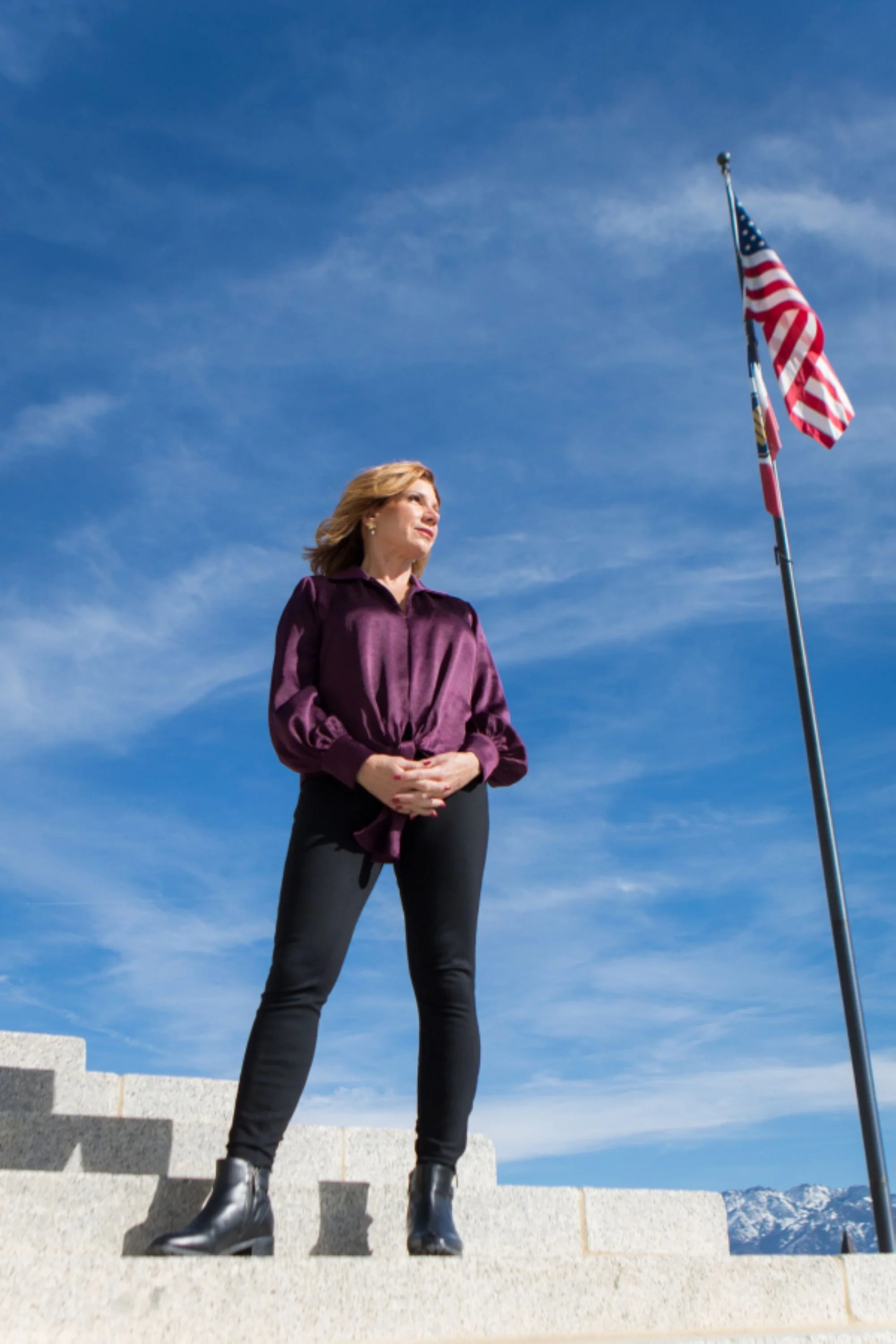 maureen farrell standing on steps in front of american flag blue skies and mountains  in background