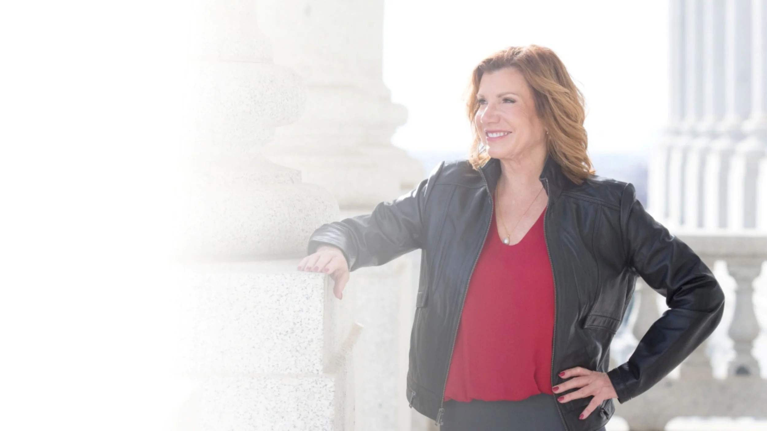 maureen farrell in red blouse black jacket smiling with arm resting on marble column
