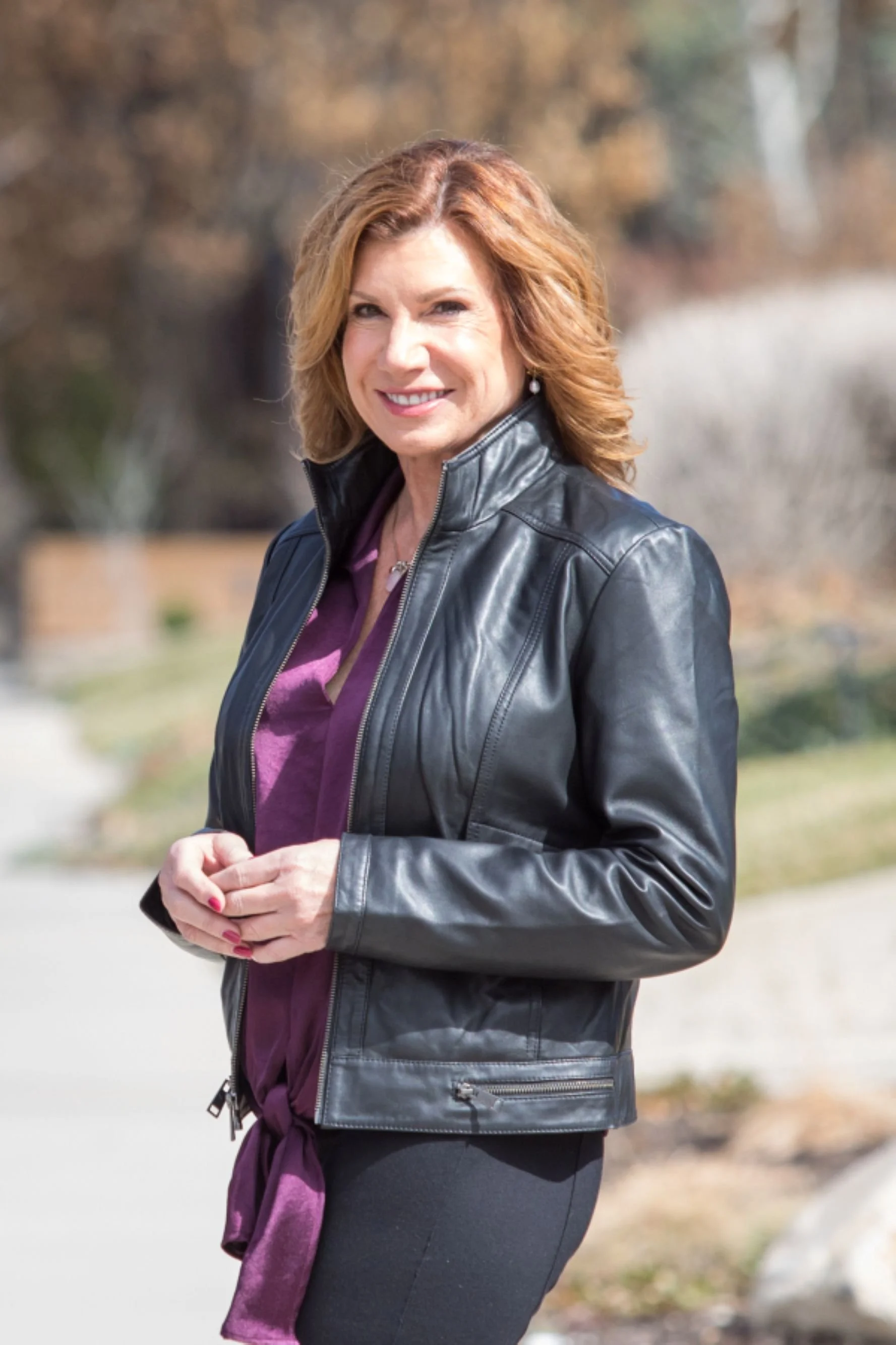 maureen farrell in black leather jacket and purple blouse standing outside smiling