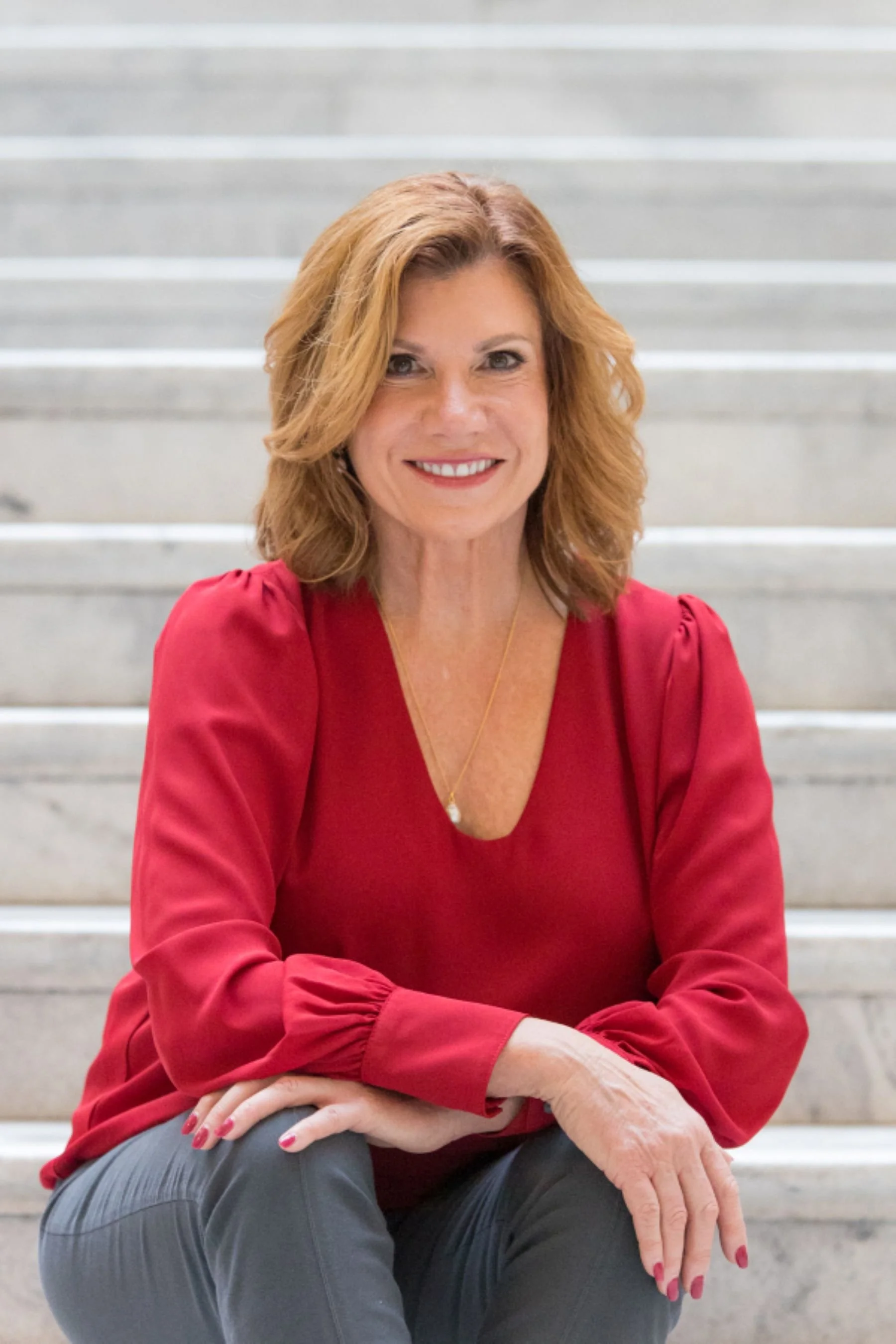 maureen farrell in red blouse sitting casually on marble steps smiling