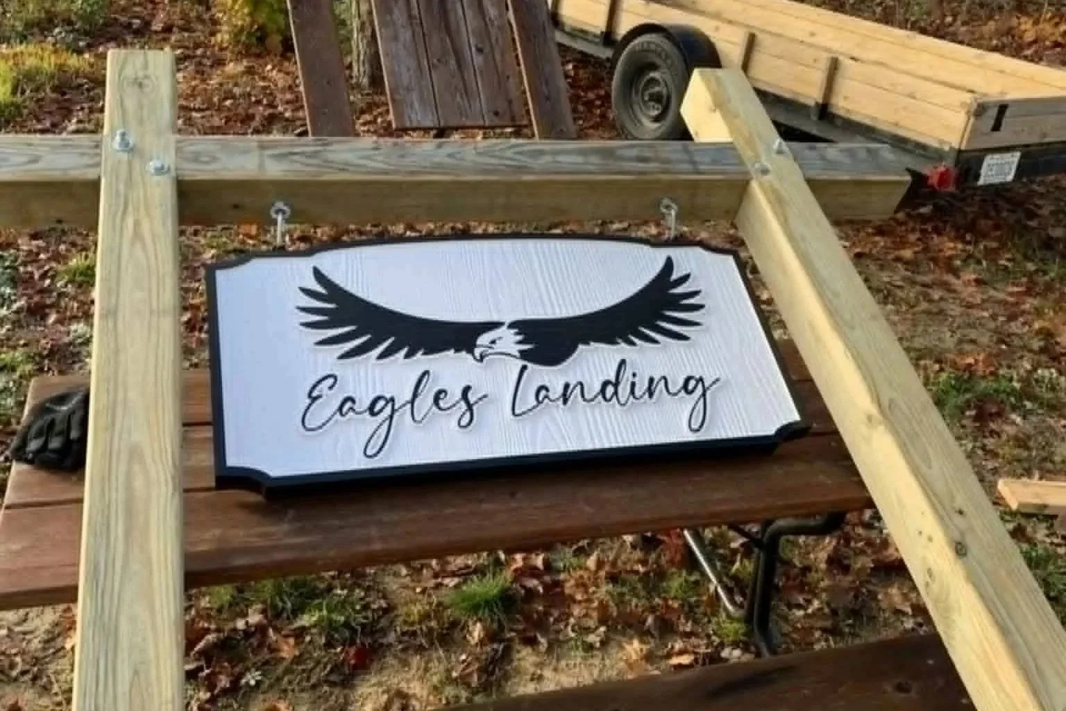 A sign with a black eagle graphic and the text 'Eagles Landing' on a white background, lying on a wooden surface outdoors with some construction materials around.