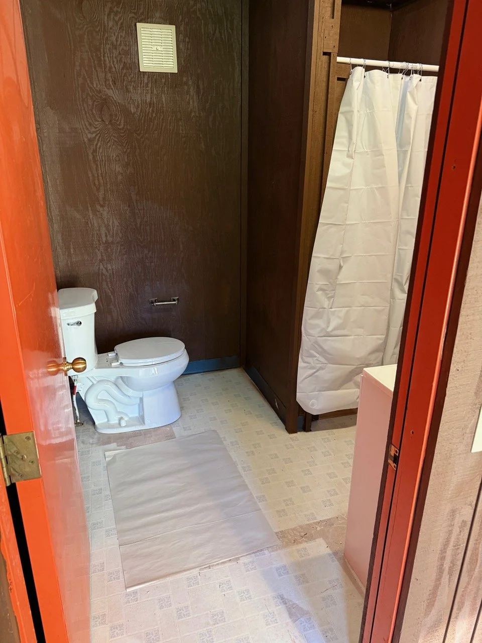 Bathroom with a toilet, shower curtain, brown wood walls, and beige tile floor.
