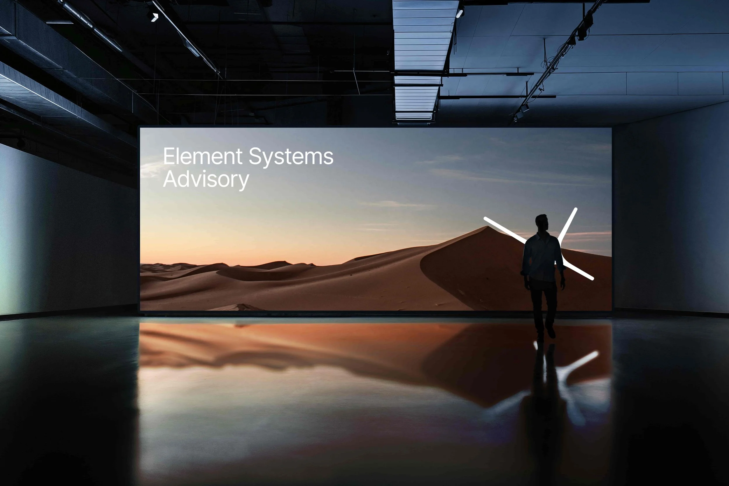 A person standing in front of a large display screen with the text 'Element Systems Advisory,' showing an image of a desert landscape at sunset.