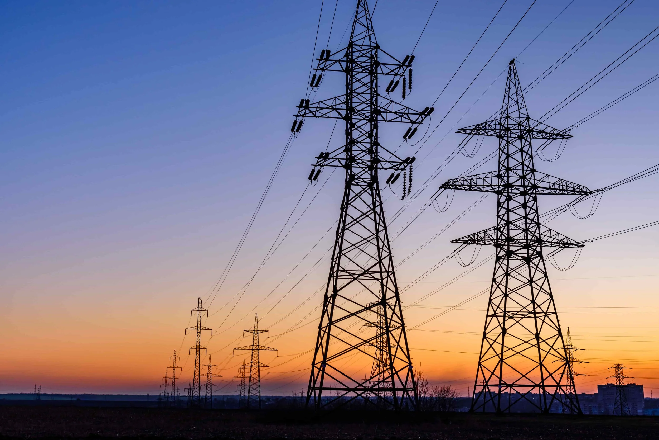A landscape with multiple electrical transmission towers silhouetted against a colorful sunset sky.