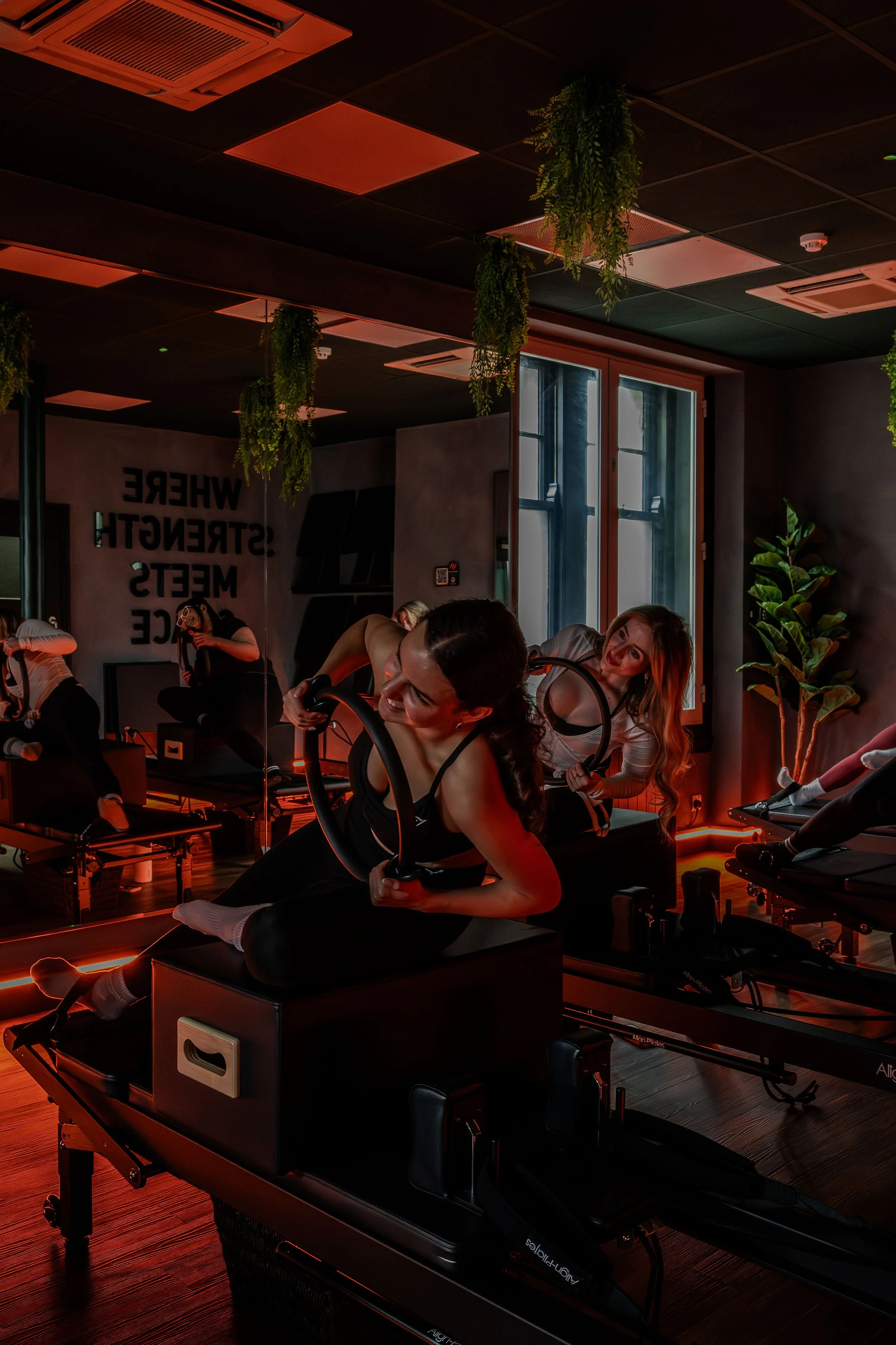 Women exercising with resistance bands in a dimly lit fitness studio with plants and mirrors.