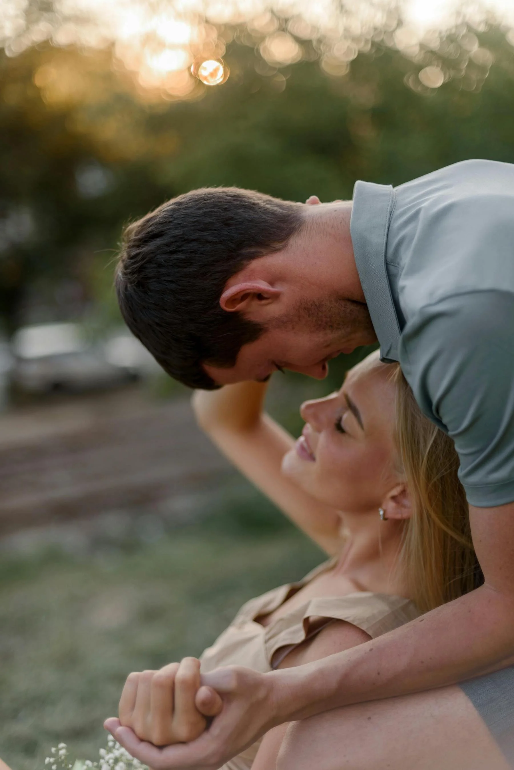 A man and woman practicing partner yoga outdoors during sunset, with their foreheads together and arms intertwined in a supportive pose.