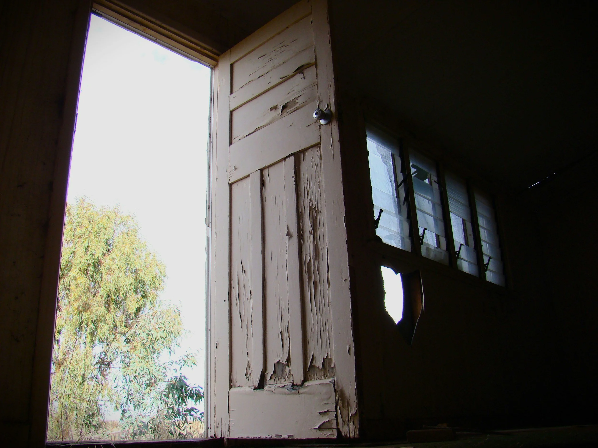 An old warped wooden exterior door and a cracked glass window frame showing structural energy leaks