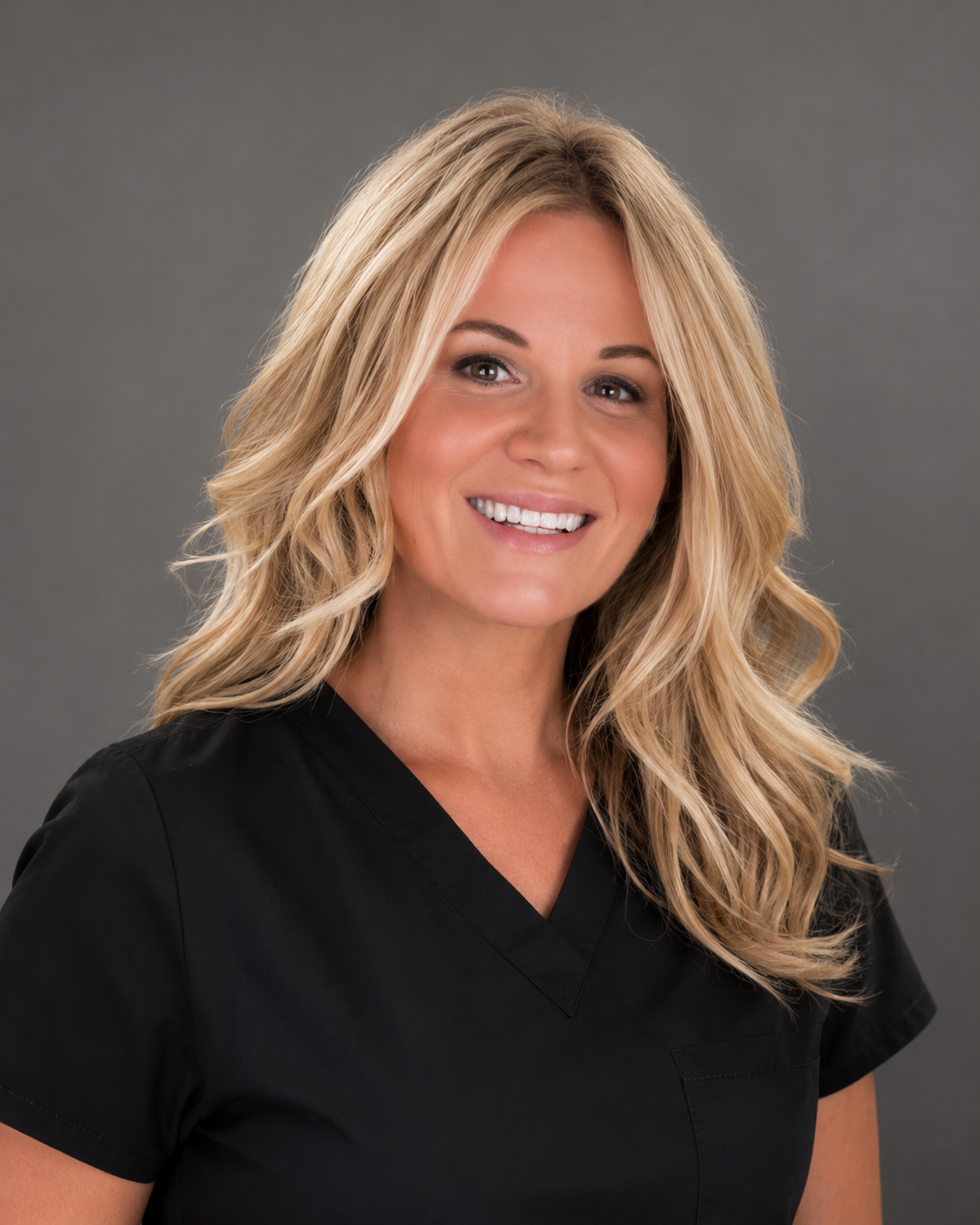 A smiling woman with long blonde wavy hair, wearing black medical scrubs, against a gray background. Skyiley Aesthetics Wellness in Sarasota, FL
