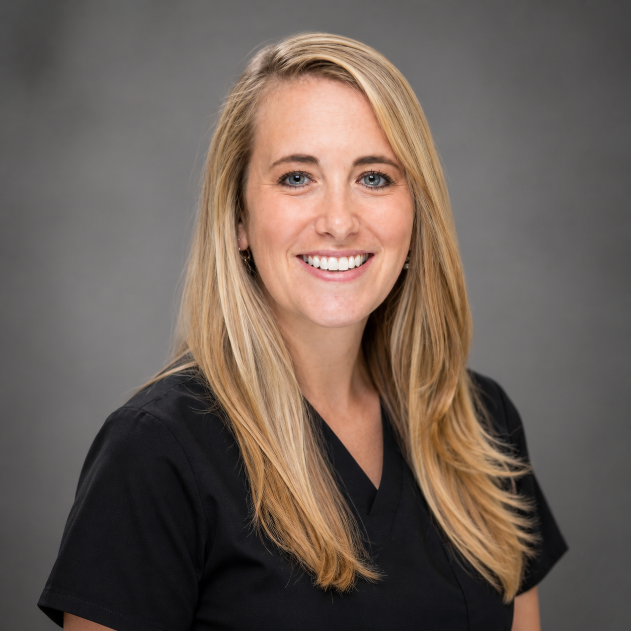 A young woman with long blonde hair, blue eyes, and a bright smile, wearing black scrubs against a gray background. Skyiley Aesthetics Wellness in Sarasota, FL
