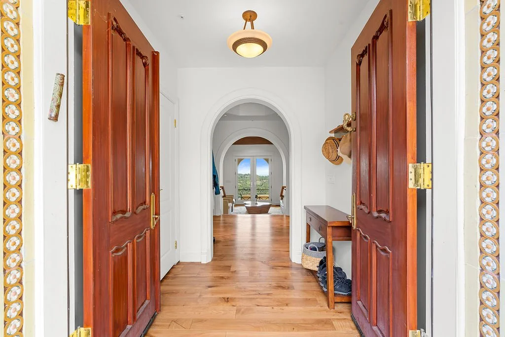 View from entrance of a home looking into a hallway with wooden double doors on either side, leading to a room with a scenic view outside.