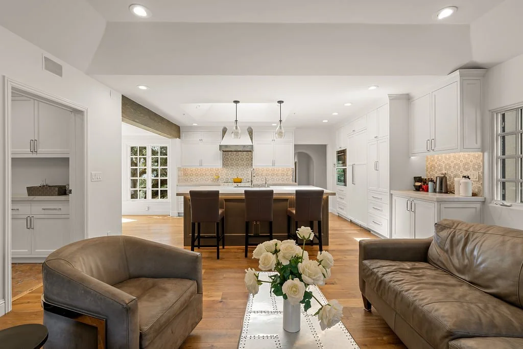 Open-concept living room and kitchen with white cabinetry, a kitchen island, brown seating, and hardwood floors.