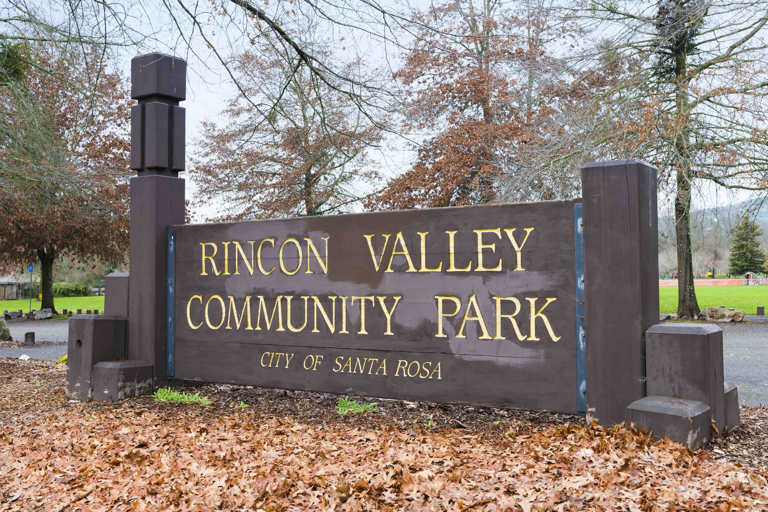 Sign at Rincon Valley Community Park in Santa Rosa, California, with trees and fallen leaves around it