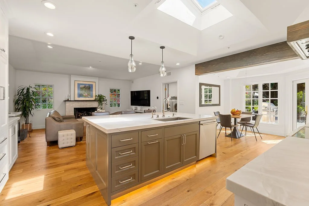 Open-concept kitchen and living room with skylights, hardwood floors, an island, dining area, and large windows.