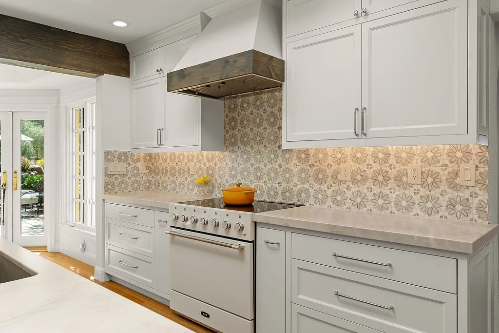 Kitchen with white cabinets, patterned tile backsplash, electric stove, and a yellow pot on the stove. There is a door with glass panels leading outside.
