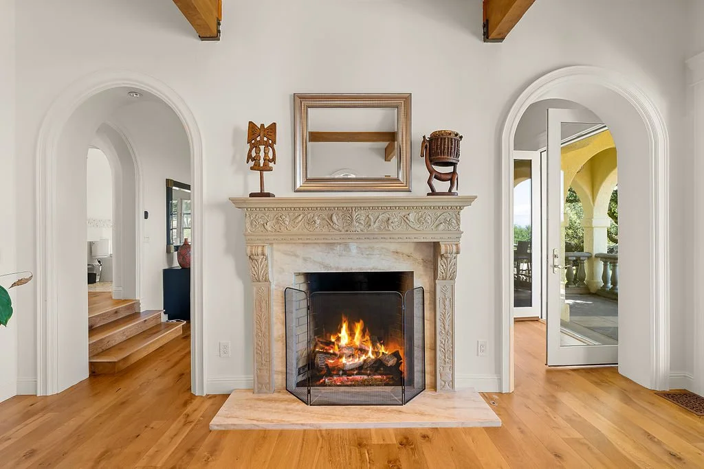Living room with a fireplace, decorative mantle, mirror, and objects on the mantle, with stairs and an open door leading to a balcony or patio.