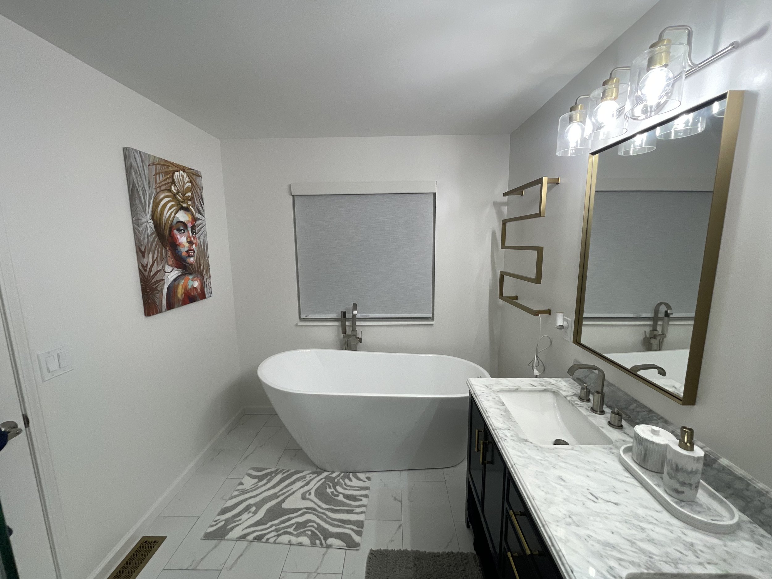 Bathroom with a bathtub, a large mirror, a marble countertop with a sink, a window with closed blinds, wall art depicting a woman's face, a modern light fixture, and a zebra print rug.
